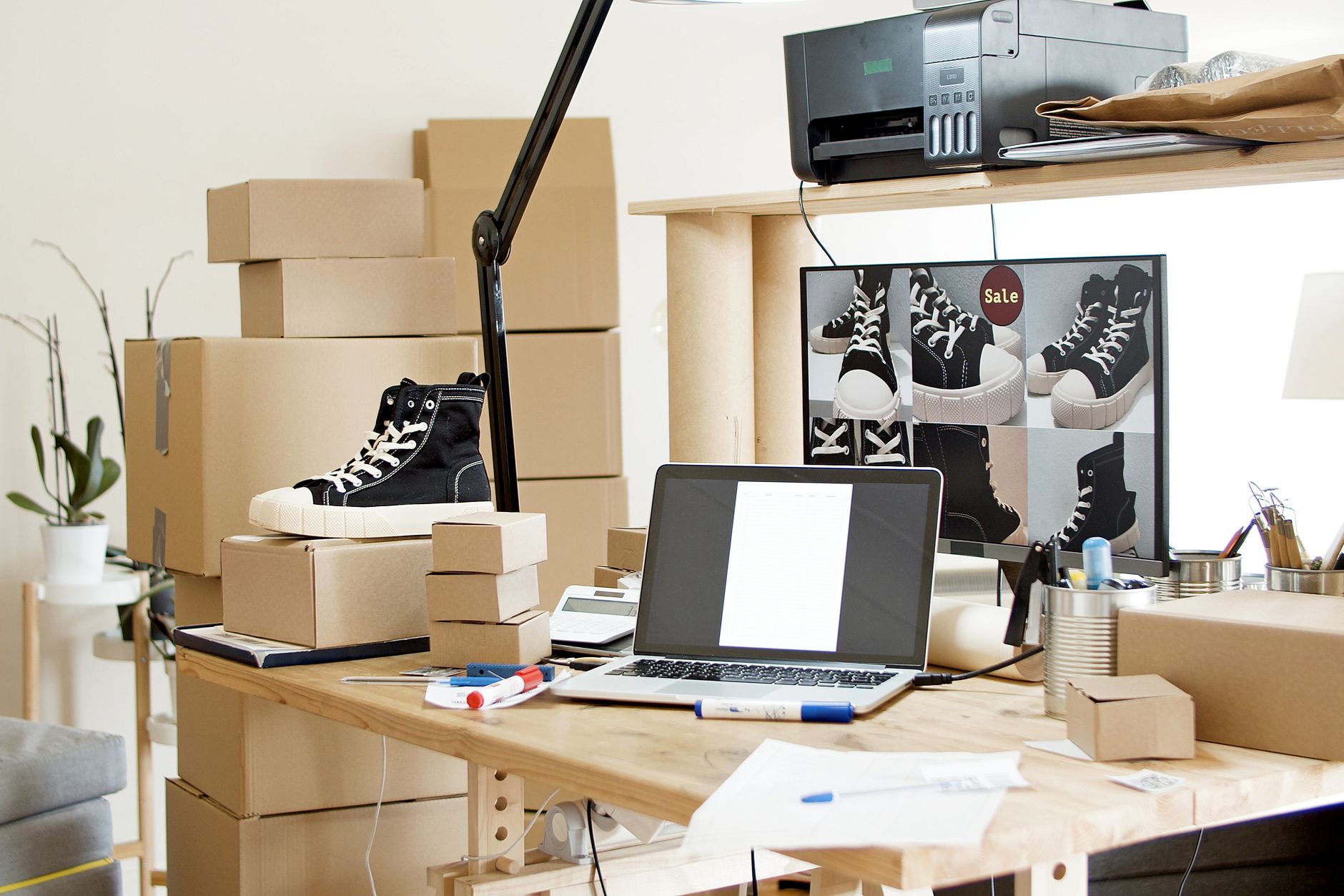 Drukke werkplek met sneakers, dozen en een laptop voor een webshopklant.